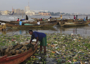 In this file photo from November 17, 2011, a fisherman stands among city trash carried in by the tide as he prepares to launch his fishing boat in Cotonou, Benin. (AP Photo/Rebecca Blackwell, File)