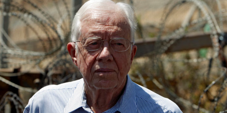 Former U.S. President Jimmy Carter is pictured standing before the contentious Israeli barrier during his visit to the West Bank village of Bilin near Ramallah on August 27, 2009. REUTERS/Ammar Awad/File Photo. Purchase Licensing Rights.