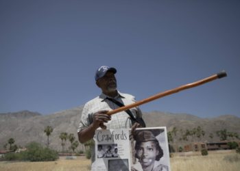 On May 30, 2024, Wendell Crawford holds up a poster featuring images of his family, who once lived in Palm Springs' Section 14 neighborhood. Pointing to the spot where his family’s home once stood, he recalled, "I used to walk through these grounds." (Zaydee Sanchez/KQED)