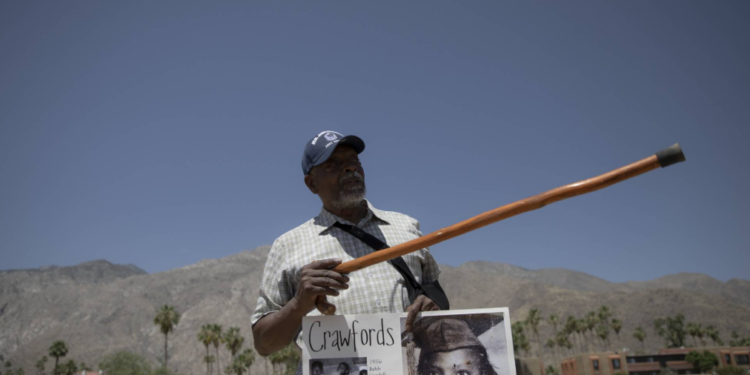 On May 30, 2024, Wendell Crawford holds up a poster featuring images of his family, who once lived in Palm Springs' Section 14 neighborhood. Pointing to the spot where his family’s home once stood, he recalled, "I used to walk through these grounds." (Zaydee Sanchez/KQED)