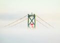 the canadian flag hangs above a suspension bridge