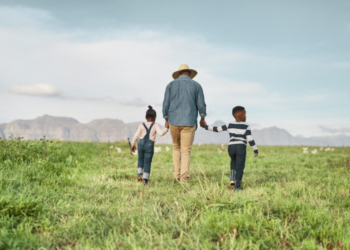 A rear view of a man with his two charming children as they explore a farm.