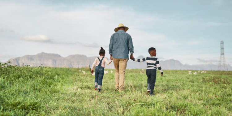 A rear view of a man with his two charming children as they explore a farm.