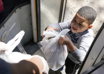 A student in Fayette, Miss., receives free meals delivered by a school bus. Amid the pandemic, buses that once carried students now serve as meal and internet access providers. These disruptions have complicated efforts to identify students at risk of homelessness. (Rogelio V. Solis/AP)