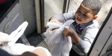 A student in Fayette, Miss., receives free meals delivered by a school bus. Amid the pandemic, buses that once carried students now serve as meal and internet access providers. These disruptions have complicated efforts to identify students at risk of homelessness. (Rogelio V. Solis/AP)