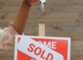 a sold signboard and a person holding keys