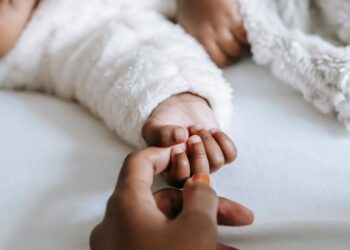 crop anonymous black mother holding hand of baby lying on bed
