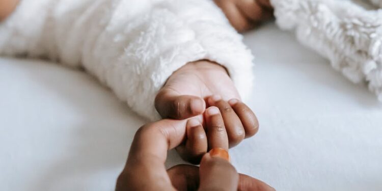 crop anonymous black mother holding hand of baby lying on bed