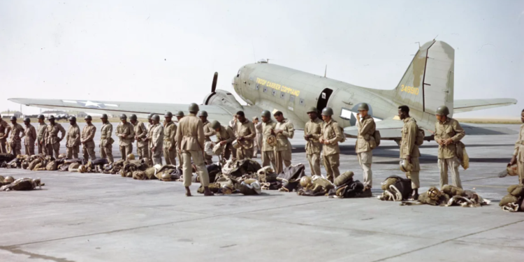 "In 1945, paratroopers of the 555th Parachute Infantry Battalion lined up in their 'jumpsuits' before embarking on a mission. Behind them stands a C-47 aircraft from the Troop Carrier Command, ready to transport them to their destination."— US National Archives